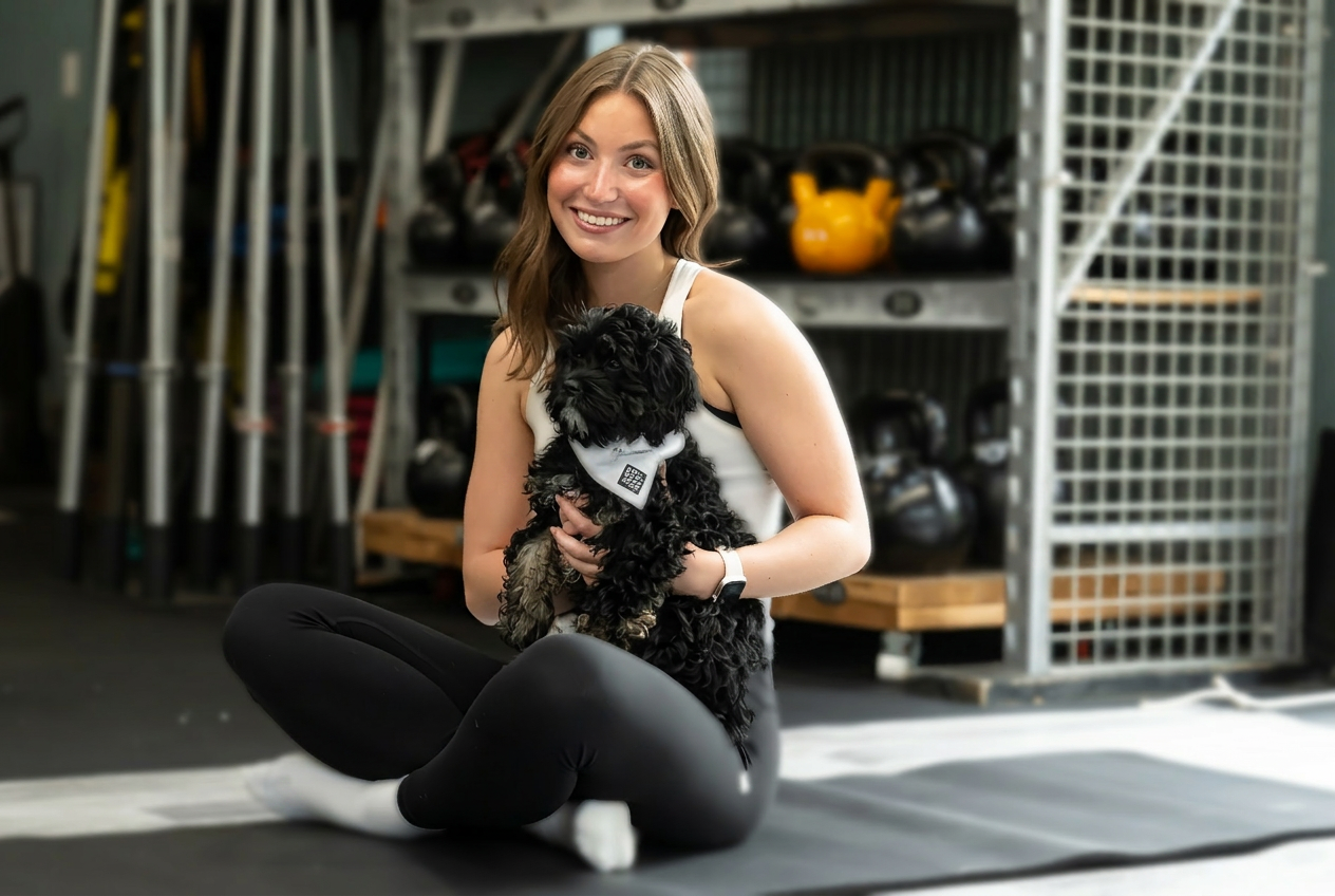 Yoga instructor smiling and holding a small black puppy on a studio mat