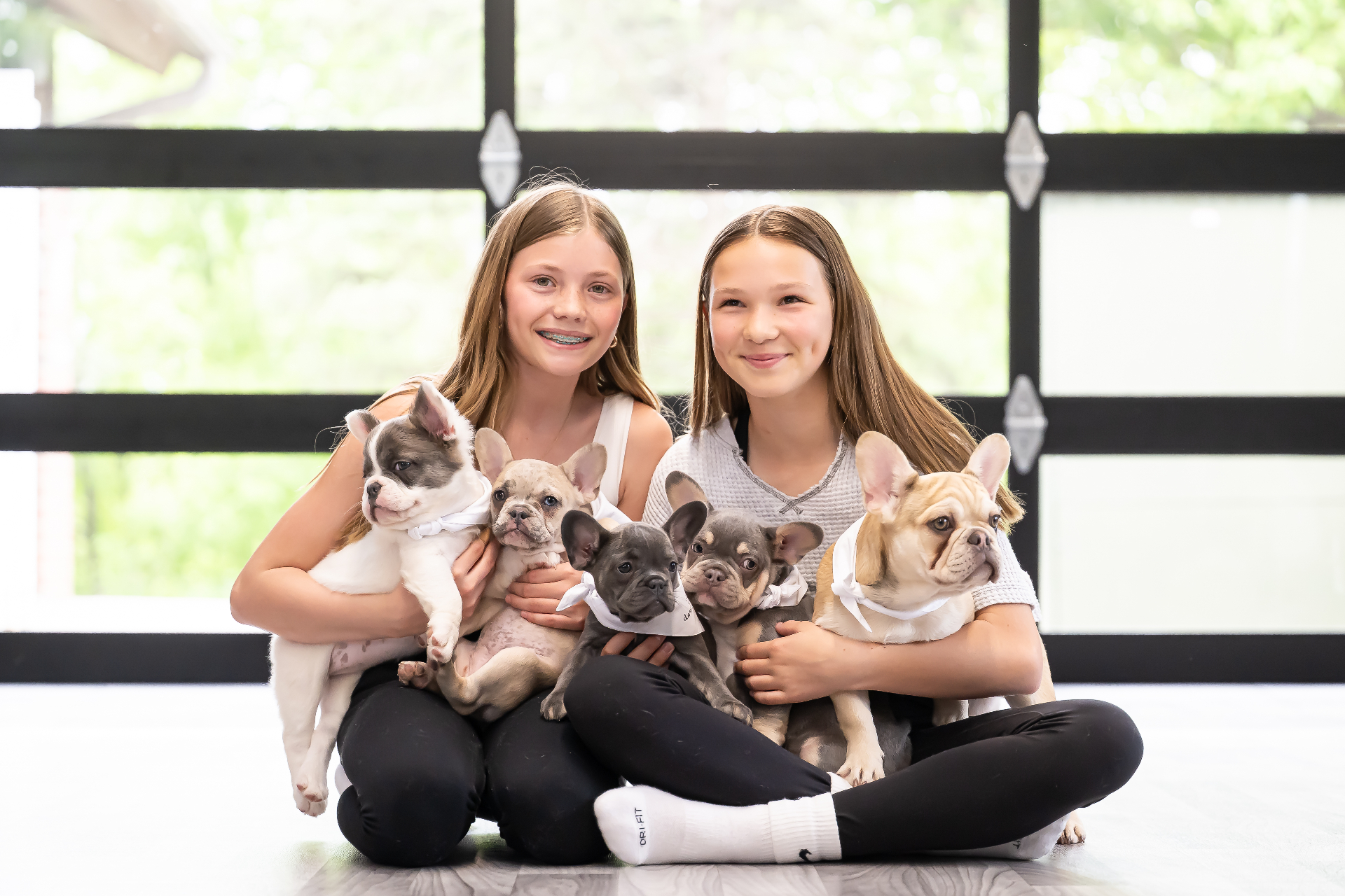 Two girls smiling while holding French bulldog puppies